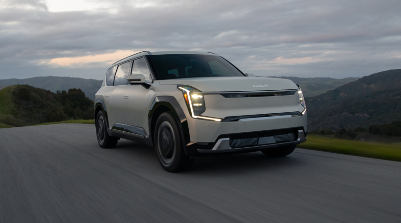 2024 Kia EV9 in ivory silver, three-quarter front view driving through the hills